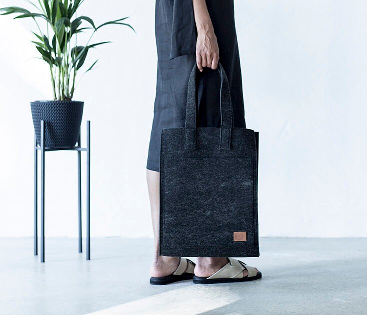 2. Close-up of woman holding Nordhale Hof Tote Bag in black, paired with a black dress and sandals