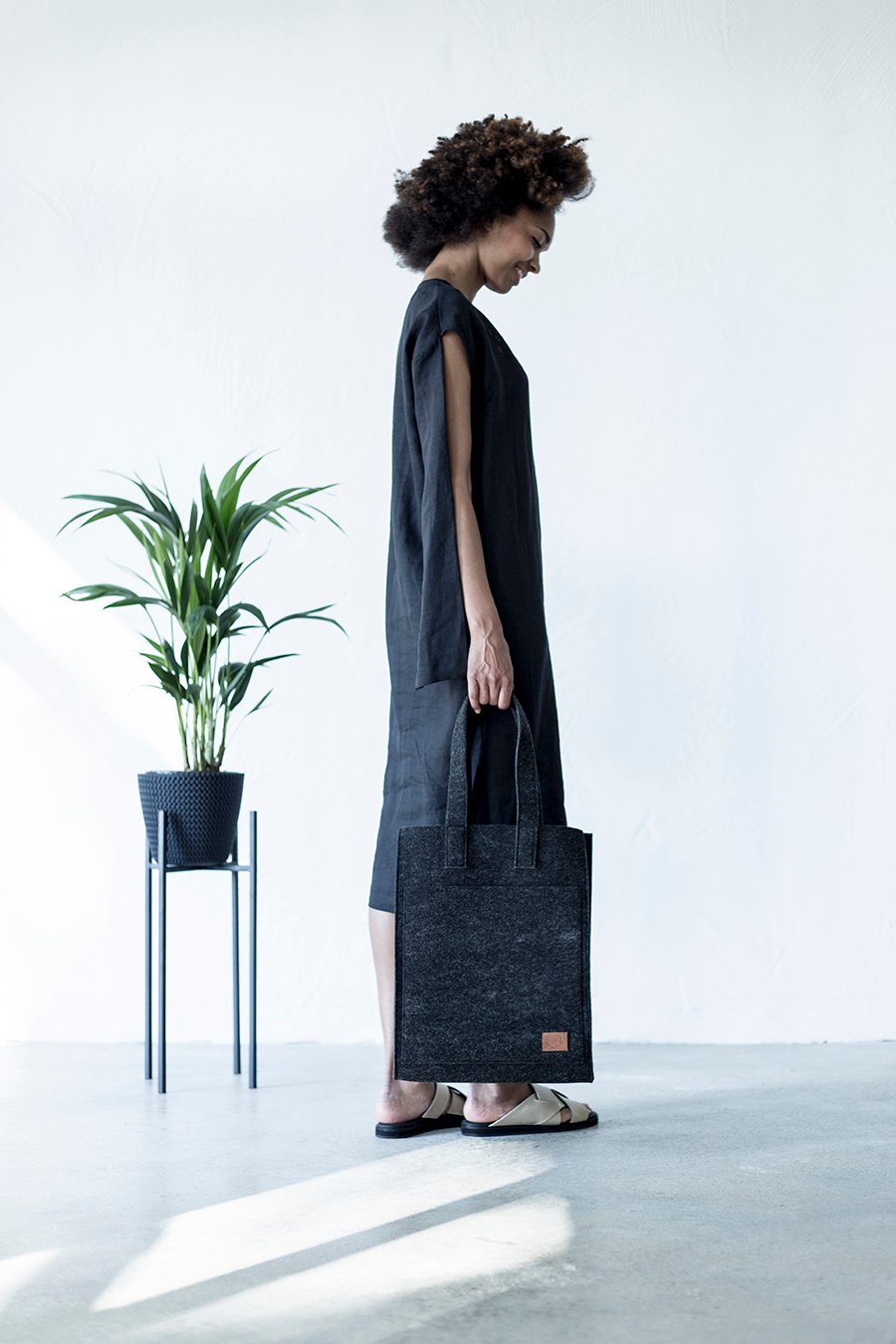 1. Woman holding Nordhale Hof Tote Bag in black, styled with a minimalist black dress in a bright room