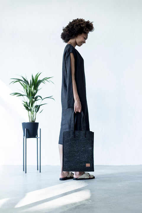 1. Woman holding Nordhale Hof Tote Bag in black, styled with a minimalist black dress in a bright room