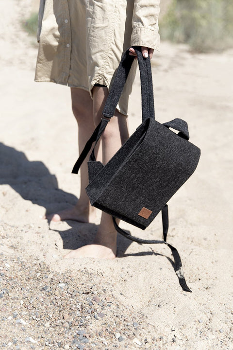 2. Woman holding Nordhale Lund Mini Backpack in black on a sandy beach