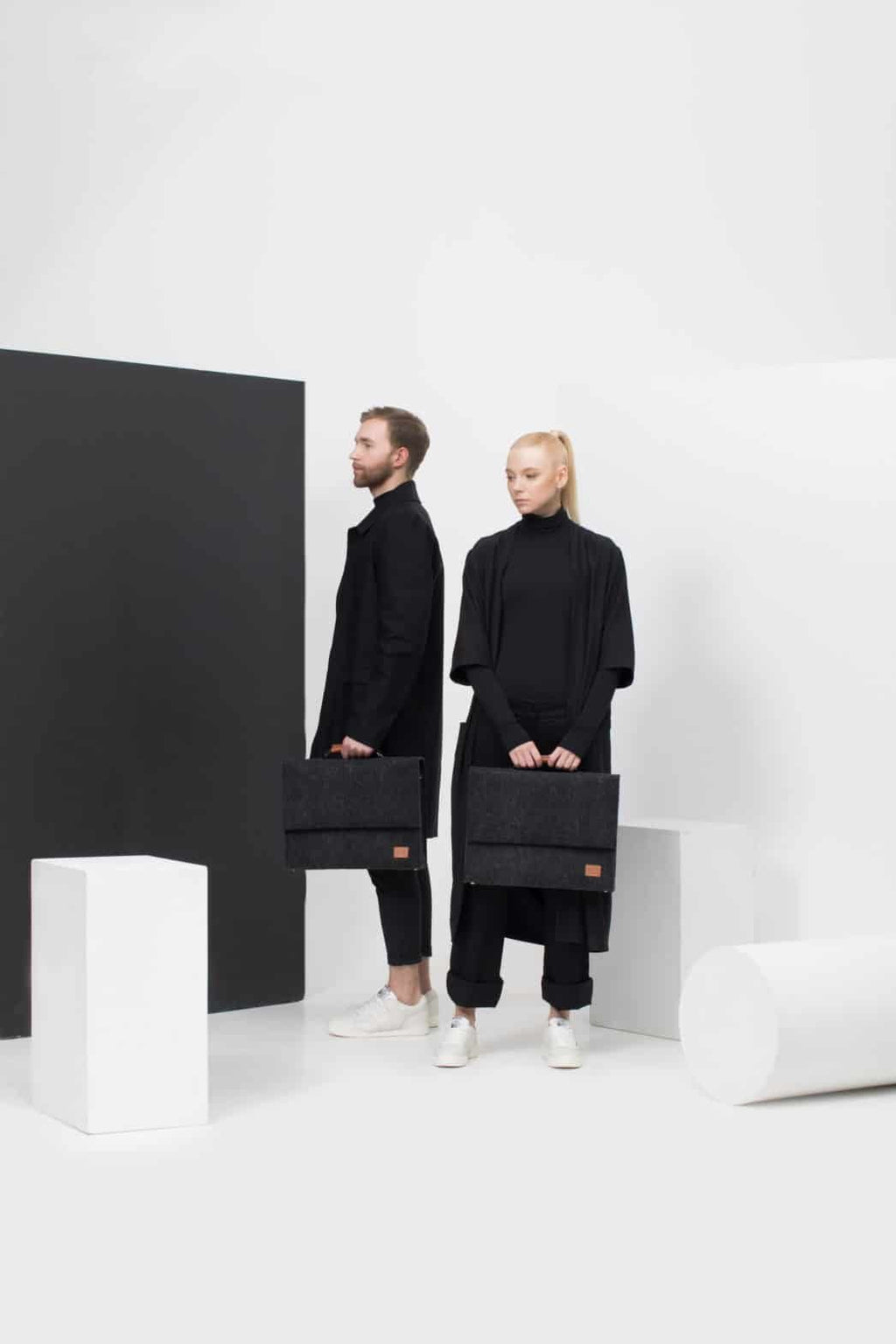 1. Unisex black Nordhale Briefcase Sören held by male and female models in a minimalist studio setting
