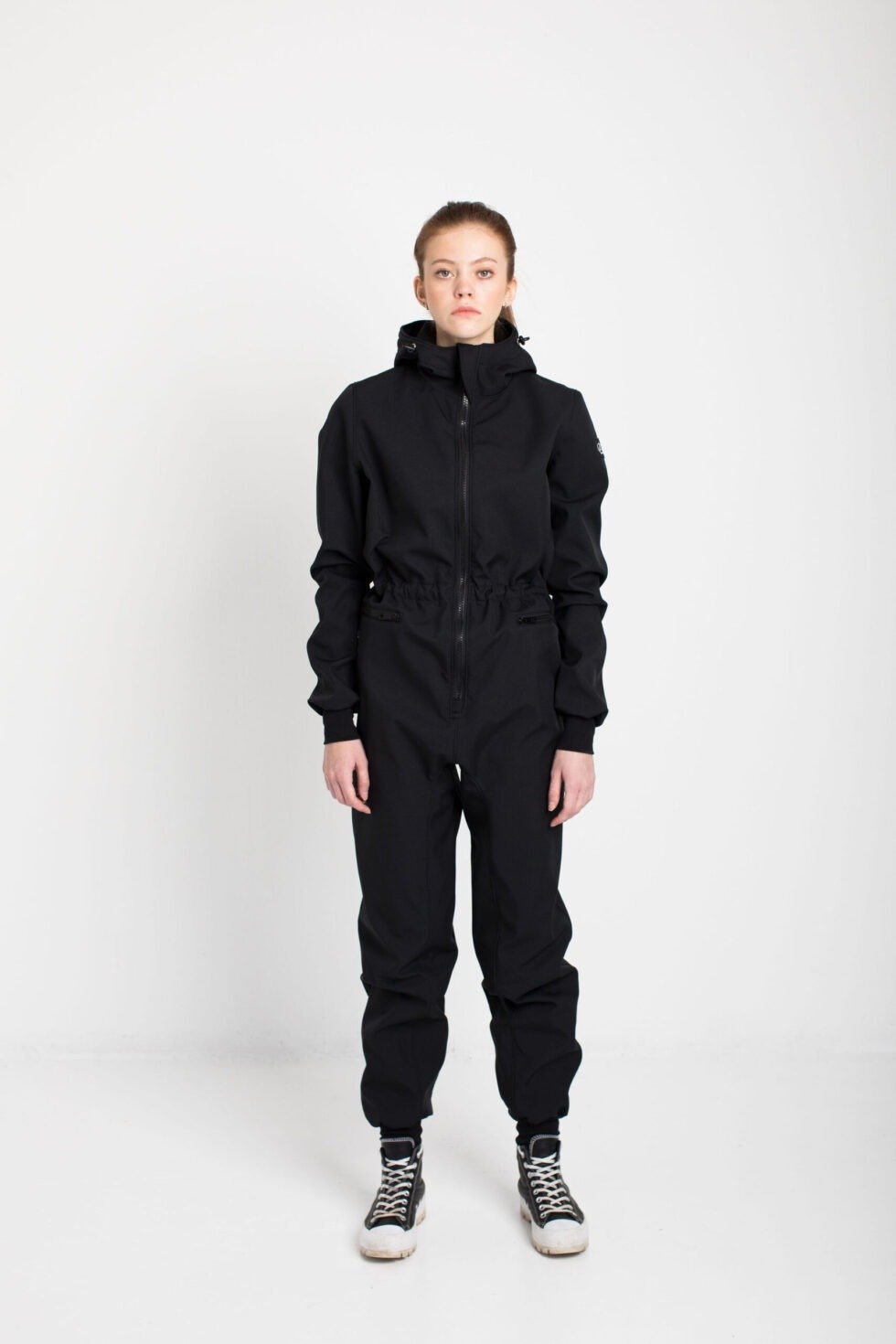 2. Women's KRISTINA softshell overall by Nuckö in black, front view in studio setting with model wearing hood