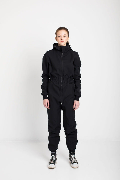 2. Women's KRISTINA softshell overall by Nuckö in black, front view in studio setting with model wearing hood
