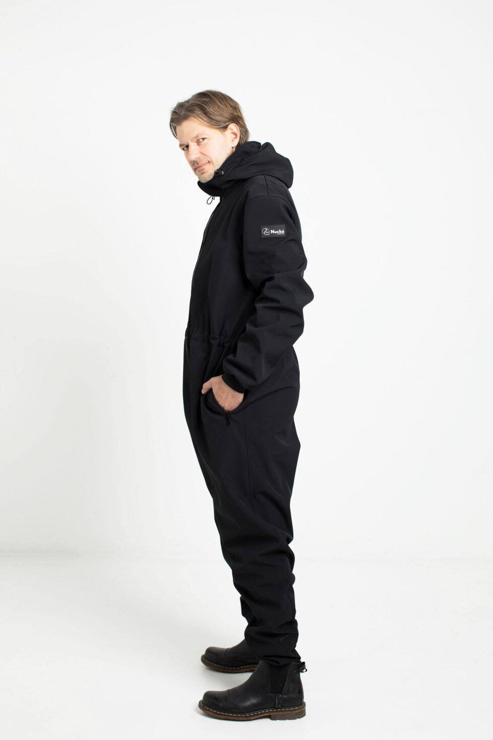 4. Man in black Nuckö RÜNNO softshell overall with hood, shown from side in studio