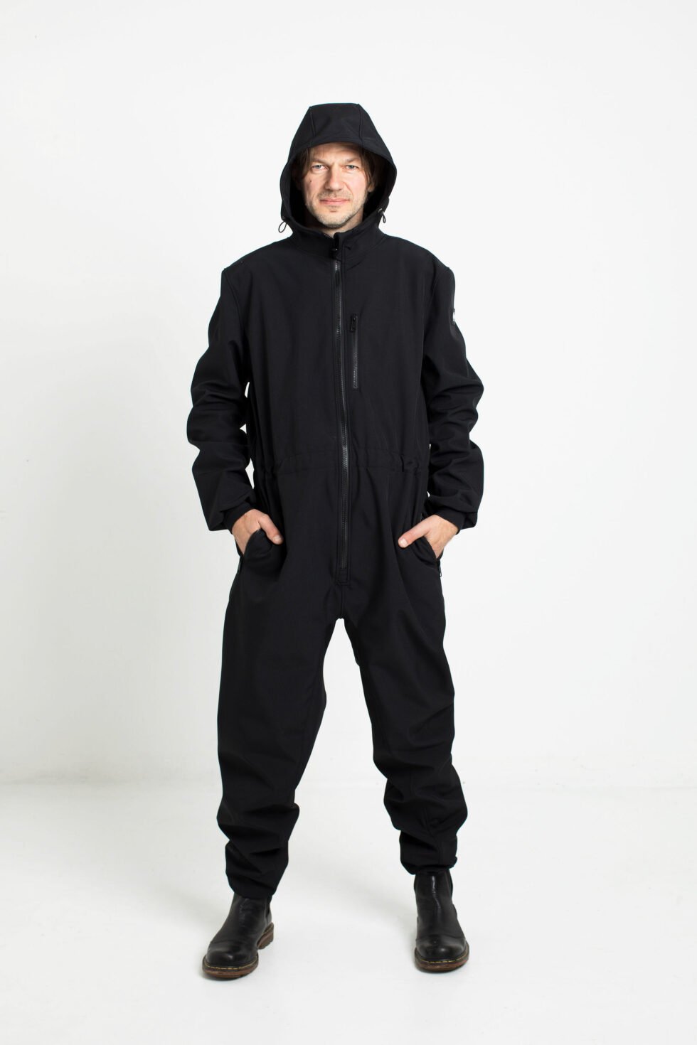1. Man wearing black Nuckö RÜNNO softshell overall with hood in studio setting