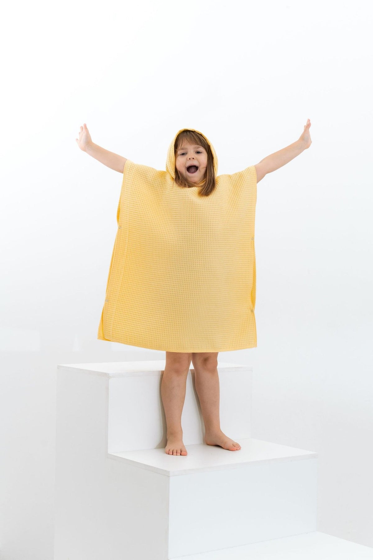 10. Girl in yellow waffle fabric poncho with hood standing with arms raised