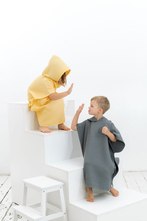 3. Two children in yellow and gray ponchos high-fiving on white steps