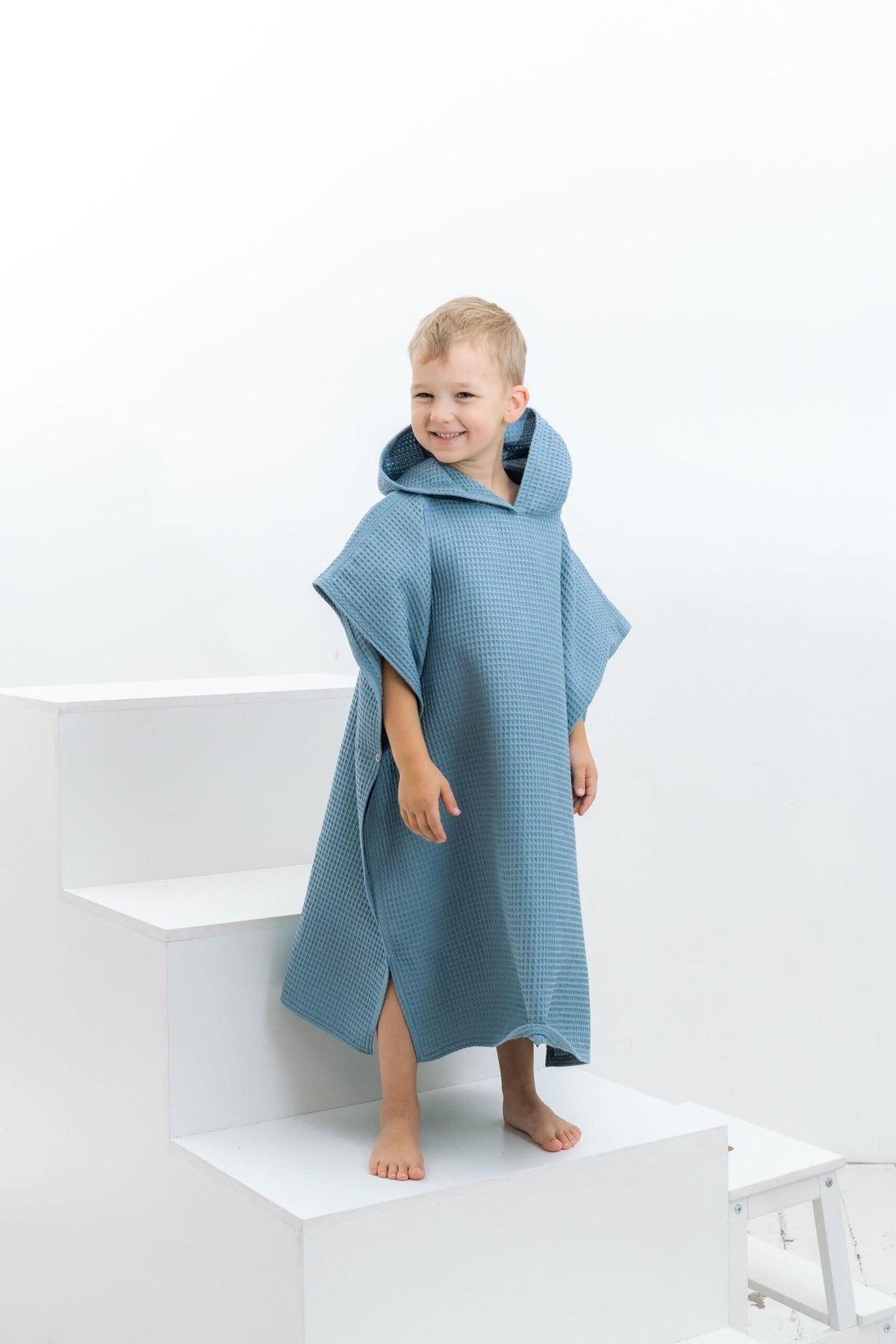 9. Boy in blue waffle fabric poncho with hood standing on white steps