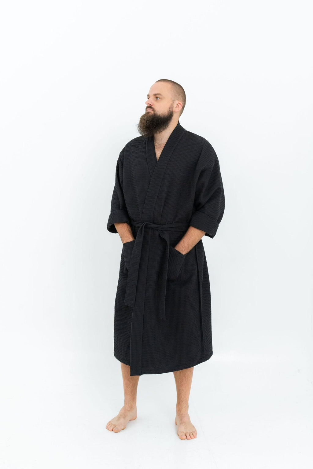 6. Man wearing black waffle fabric robe with belt and side pockets looking to the side on white background
