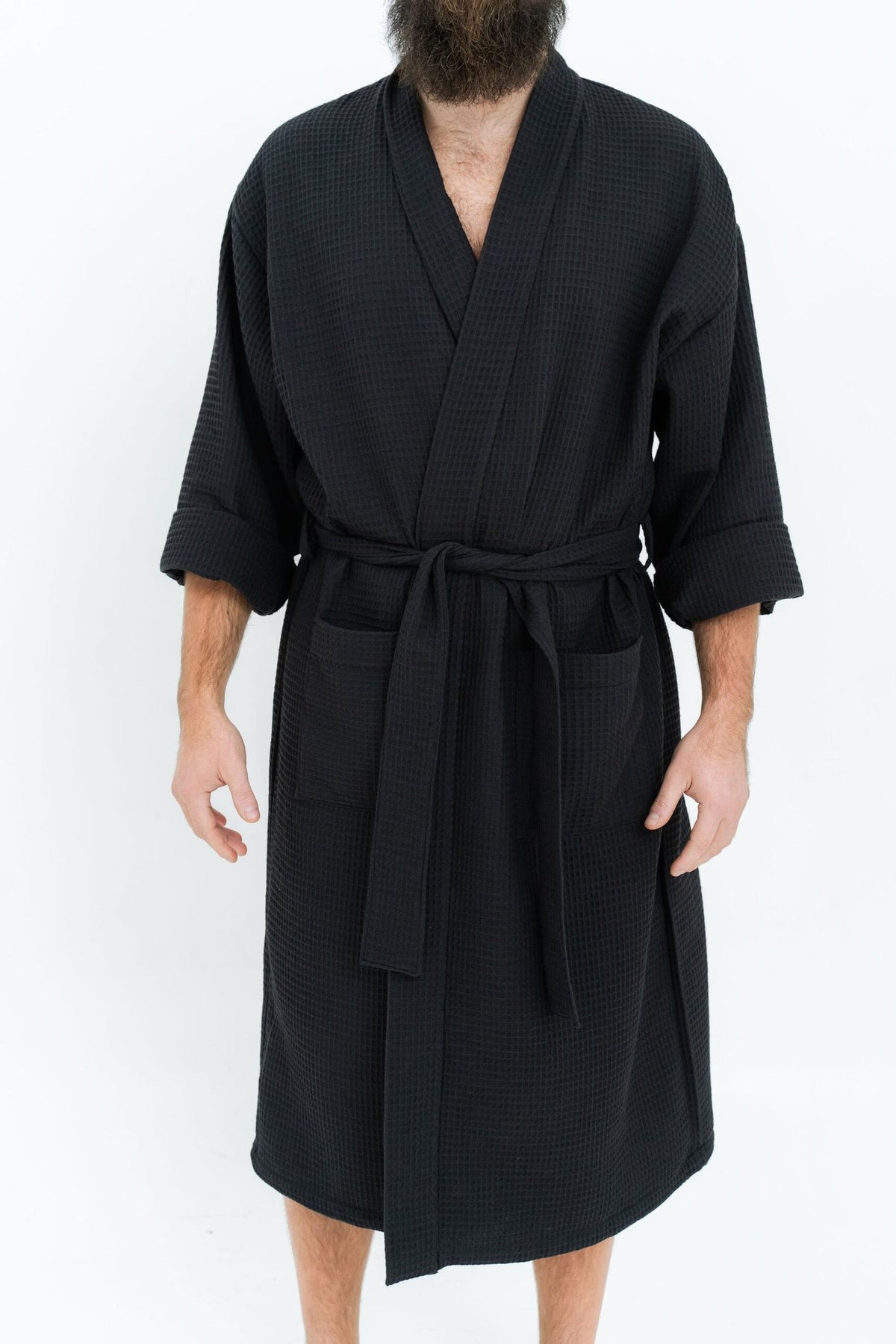 8. Man wearing black waffle fabric robe with belt and side pockets shown from front on white background