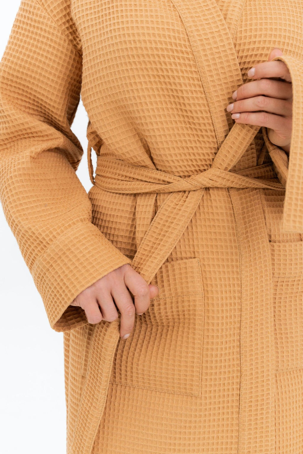 3. Close-up of woman tying belt on mustard waffle fabric robe, showing texture and pocket detail