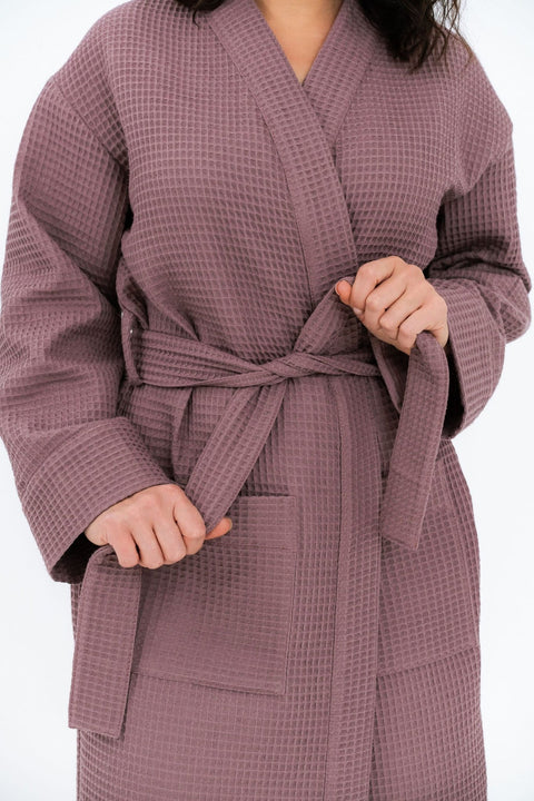 3. Close-up of woman tying belt on mauve waffle fabric robe, showing texture and pocket detail