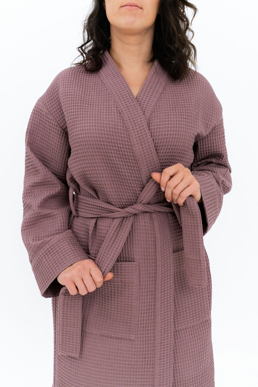 3. Close-up of woman tying belt on mauve waffle fabric robe, showing texture and pocket detail