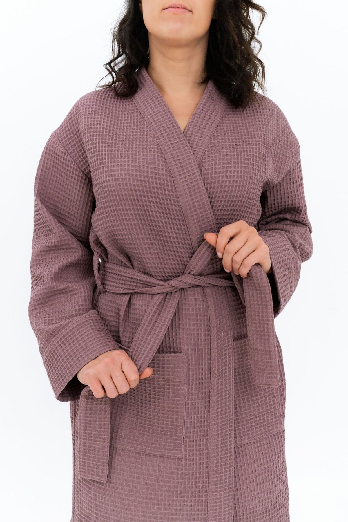 3. Close-up of woman tying belt on mauve waffle fabric robe, showing texture and pocket detail