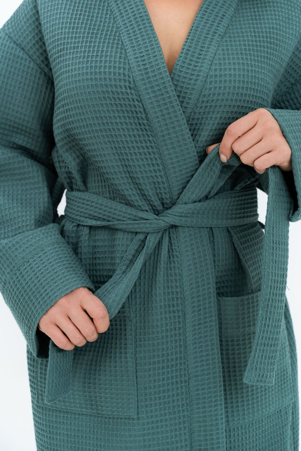3. Close-up of woman tying belt on teal waffle fabric robe, showing texture and pocket detail