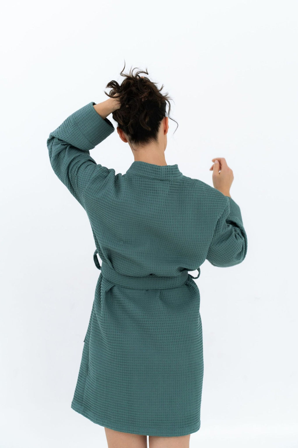 10. Woman in green waffle robe with belt, shown from back with hand in hair, studio setting