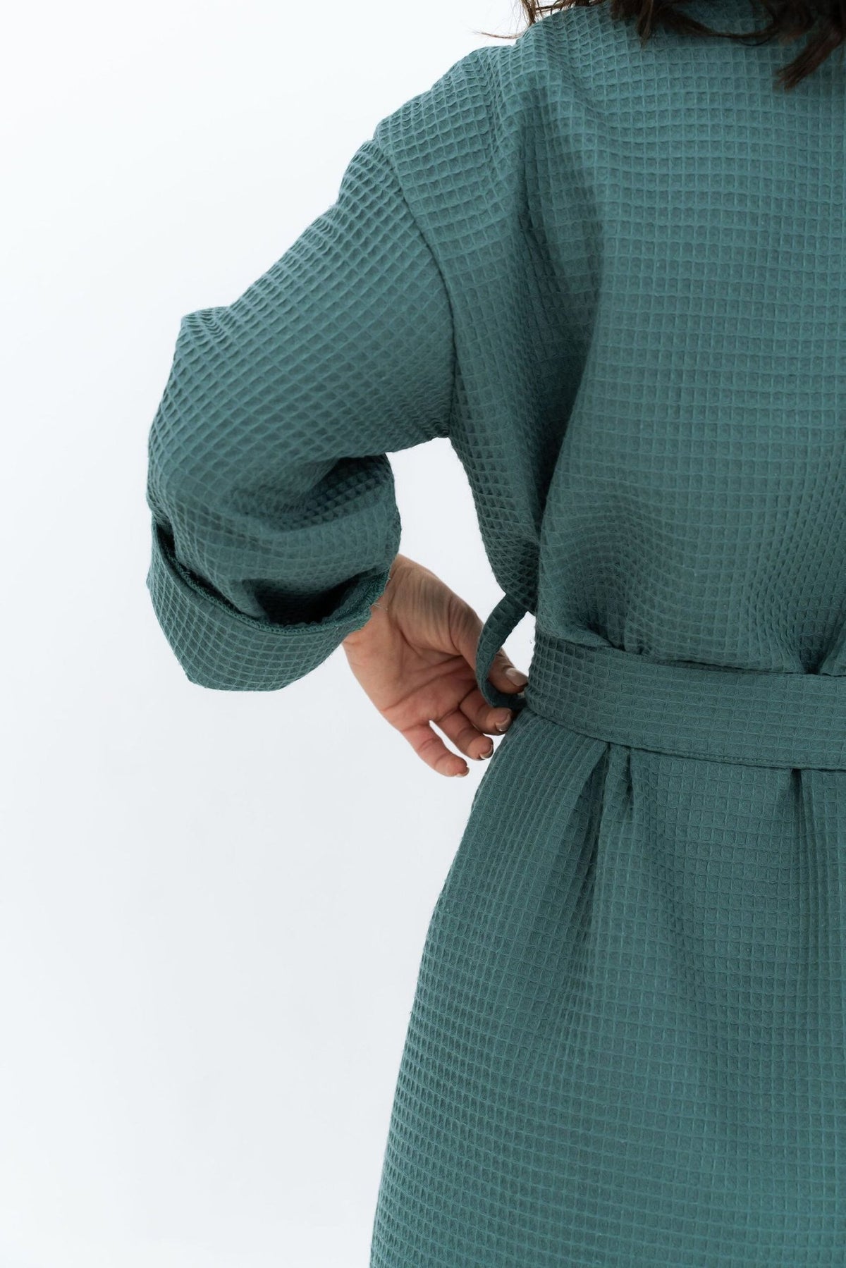 3. Back view of woman adjusting belt on teal waffle fabric robe, highlighting texture