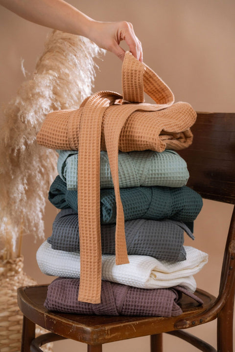 5. Stack of folded waffle robes in various colors on chair, hand holding belt