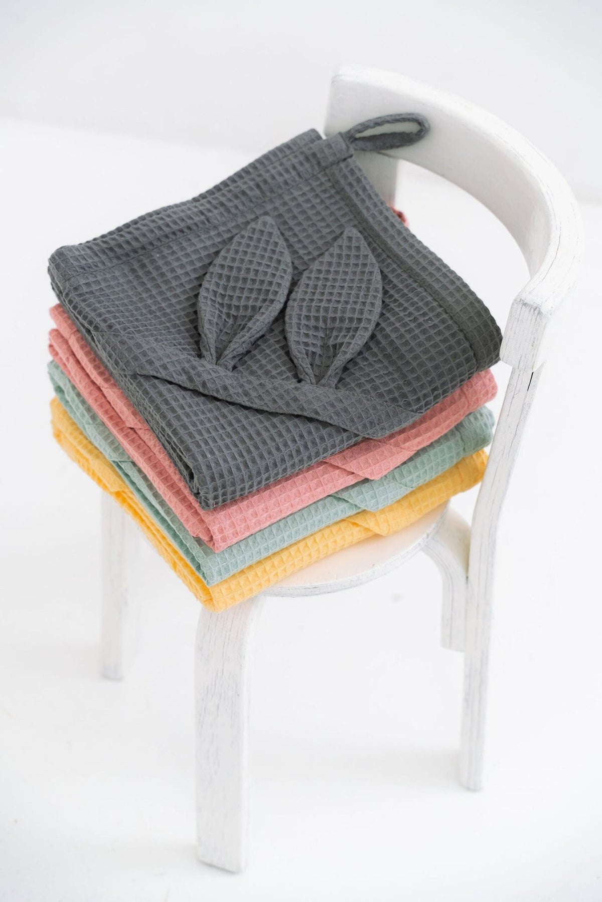 7. Stack of waffle fabric towels with bunny ears on chair in gray, pink, green, yellow, and blue