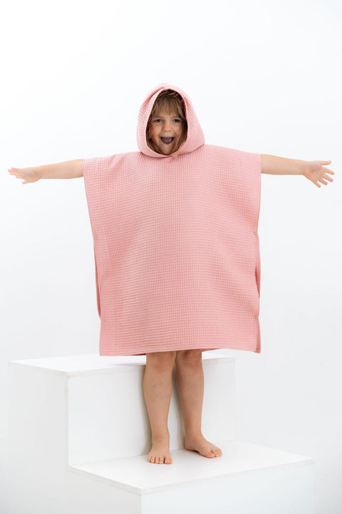 4. Child in pink waffle fabric poncho with arms outstretched on white steps