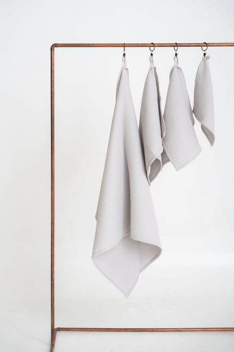 2. Light gray organic waffle cotton towels in four sizes hanging on copper rod against white background