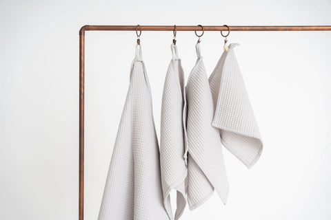 1. Set of four light gray organic waffle cotton towels hanging on copper rod, showcasing different sizes with hanging loops