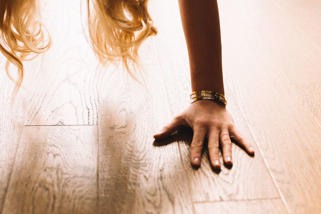 1. Woman wearing Olla 'Choose Joy' bracelet in gold, shown in a lifestyle setting with hand on wooden floor
