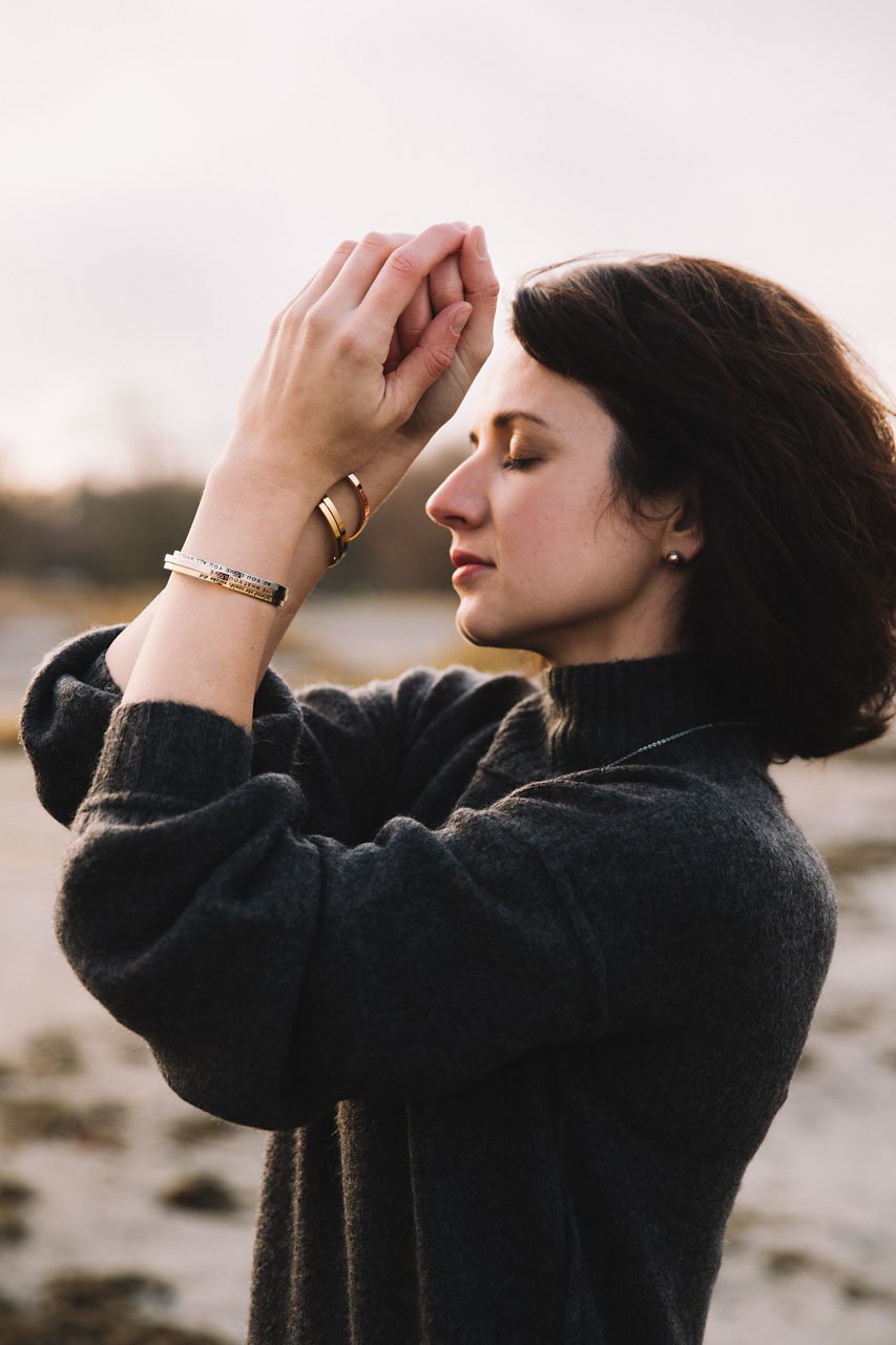 4. Woman meditating on the beach wearing Olla VHENGITÄ NAUTI OLE bracelets in silver, rose gold, and gold