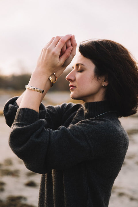 4. Woman meditating on the beach wearing Olla VHENGITÄ NAUTI OLE bracelets in silver, rose gold, and gold