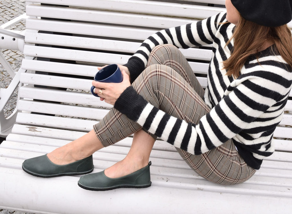 1. Woman wearing Omaking Kuutsid dark green shoes, sitting on a bench with a striped sweater and plaid pants, holding a cup