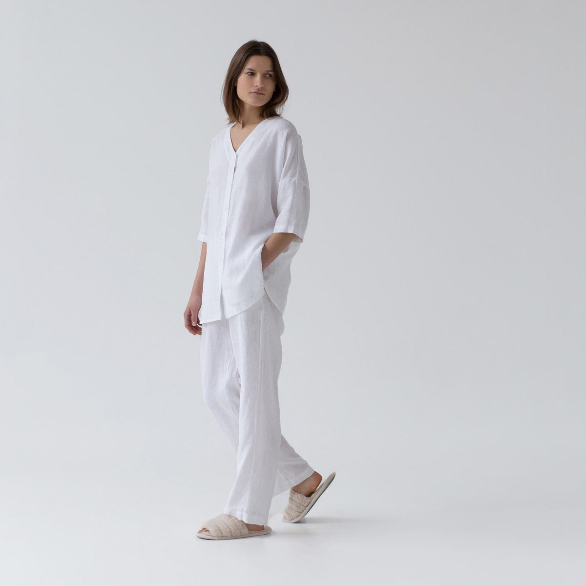 3. Woman walking in optical white linen loungewear set with V-neck shirt and relaxed pants, side view