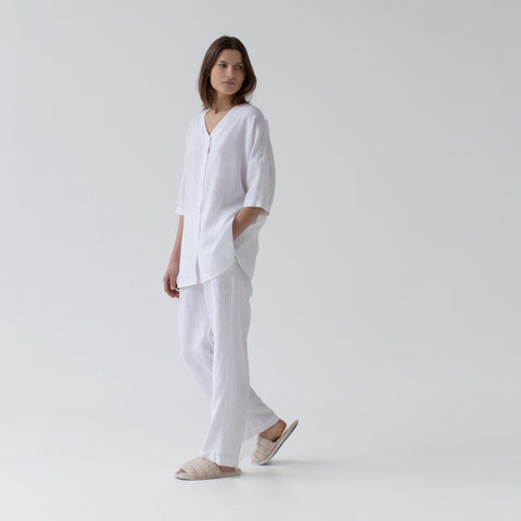 3. Woman walking in optical white linen loungewear set with V-neck shirt and relaxed pants, side view