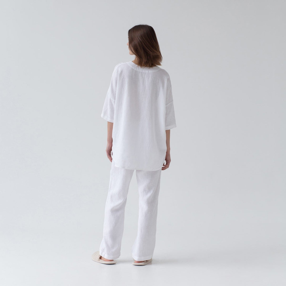 4. Back view of woman in optical white linen loungewear set with V-neck shirt and relaxed pants