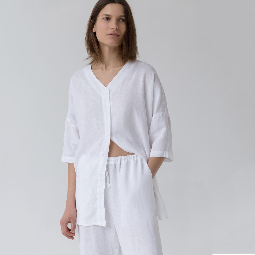 2. Woman in optical white linen loungewear set with V-neck shirt partially unbuttoned, showing relaxed fit