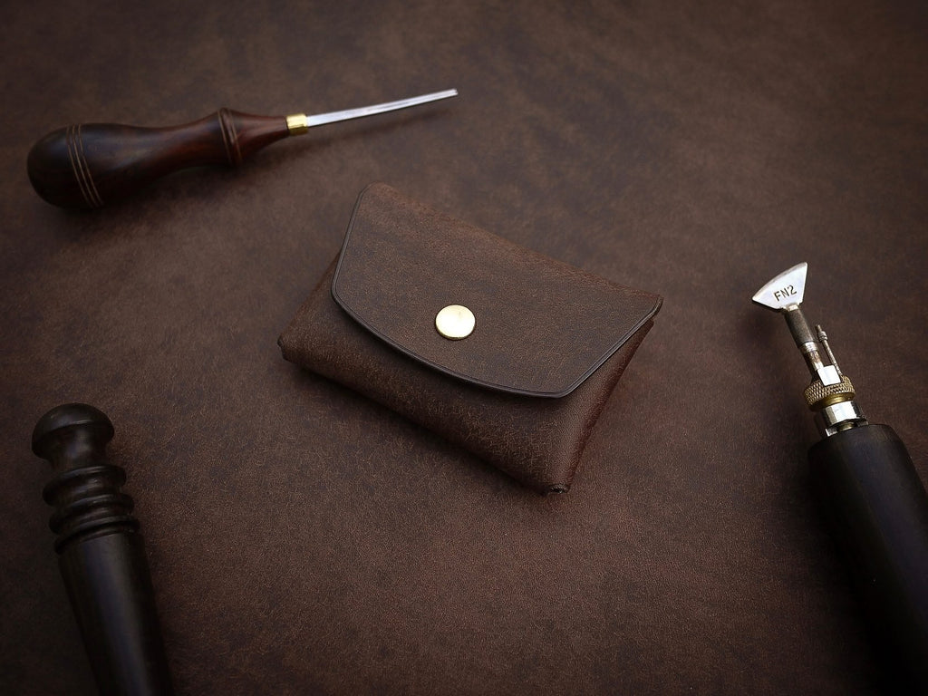 6. Mirgoods dark brown button leather wallet with brass snap, displayed with leather crafting tools