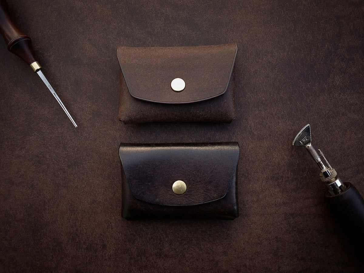 2. Two Mirgoods dark brown button leather wallets with brass snaps, displayed with leather crafting tools