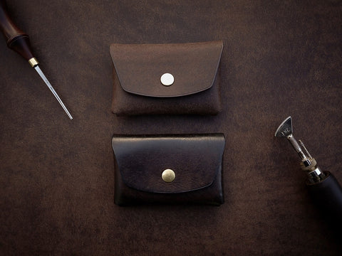 2. Two Mirgoods dark brown button leather wallets with brass snaps, displayed with leather crafting tools