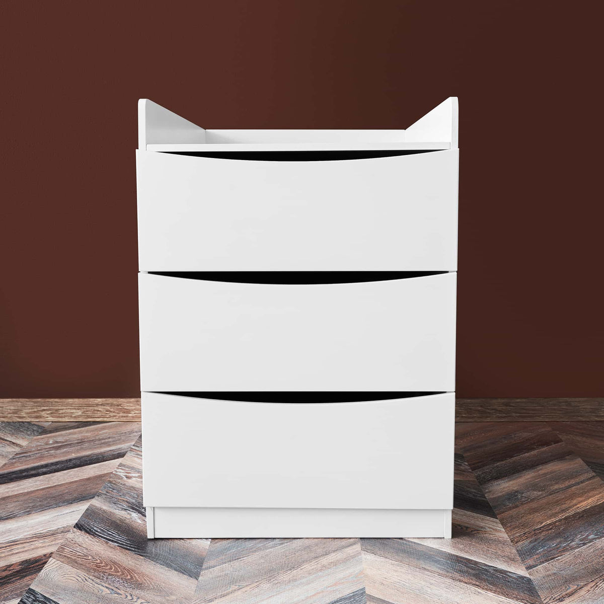 3. White chest of drawers with three drawers on dark wood floor and brown background