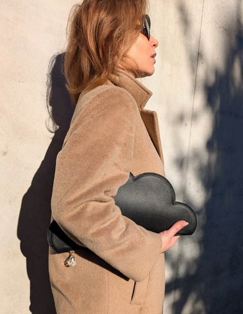 2. Woman in beige coat carrying Tairi Roosve Leather Clutch Bag Cloud in black, side profile view