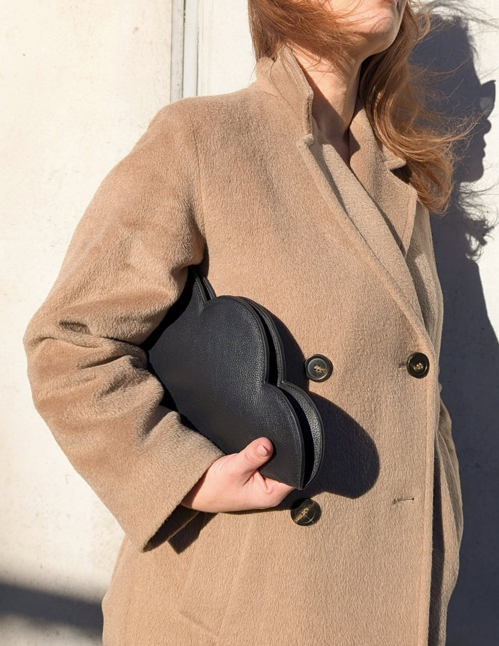 7. Woman in beige coat holding Tairi Roosve Leather Clutch Bag Cloud in black, front view