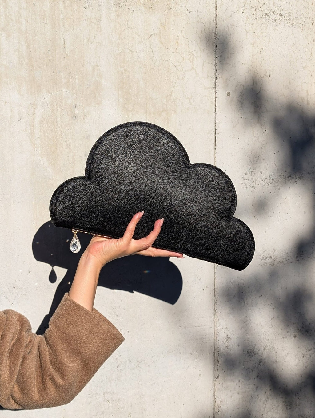 1. Woman holding Tairi Roosve Leather Clutch Bag Cloud in black, showcasing raindrop zip detail against a concrete wall