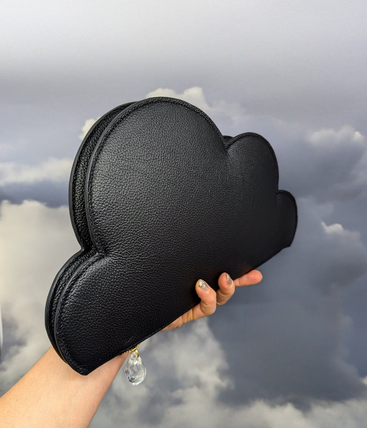 5. Tairi Roosve Leather Clutch Bag Cloud in black held against a cloudy sky background, emphasizing design and raindrop detail