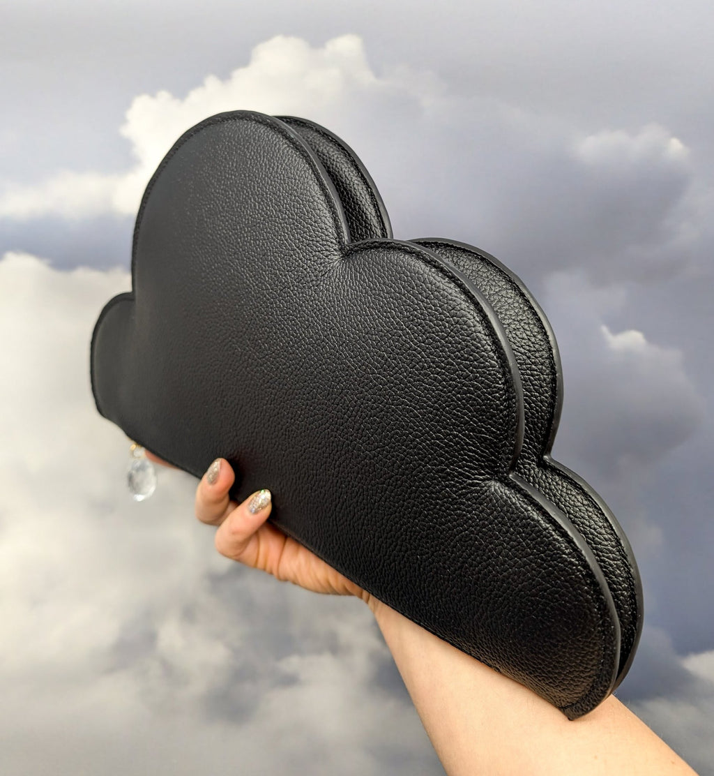 6. Tairi Roosve Leather Clutch Bag Cloud in black held up against a cloudy sky, highlighting unique shape