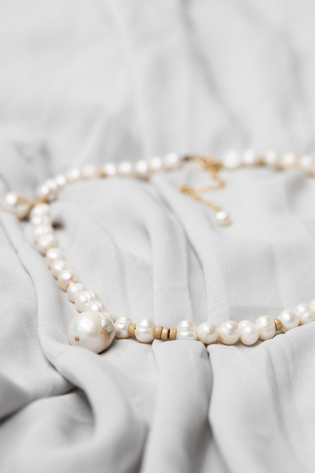 2. Close-up of New Vintage by Kriss custom-made pearl necklace featuring Baroque pearls and gold-filled accents on a soft fabric background