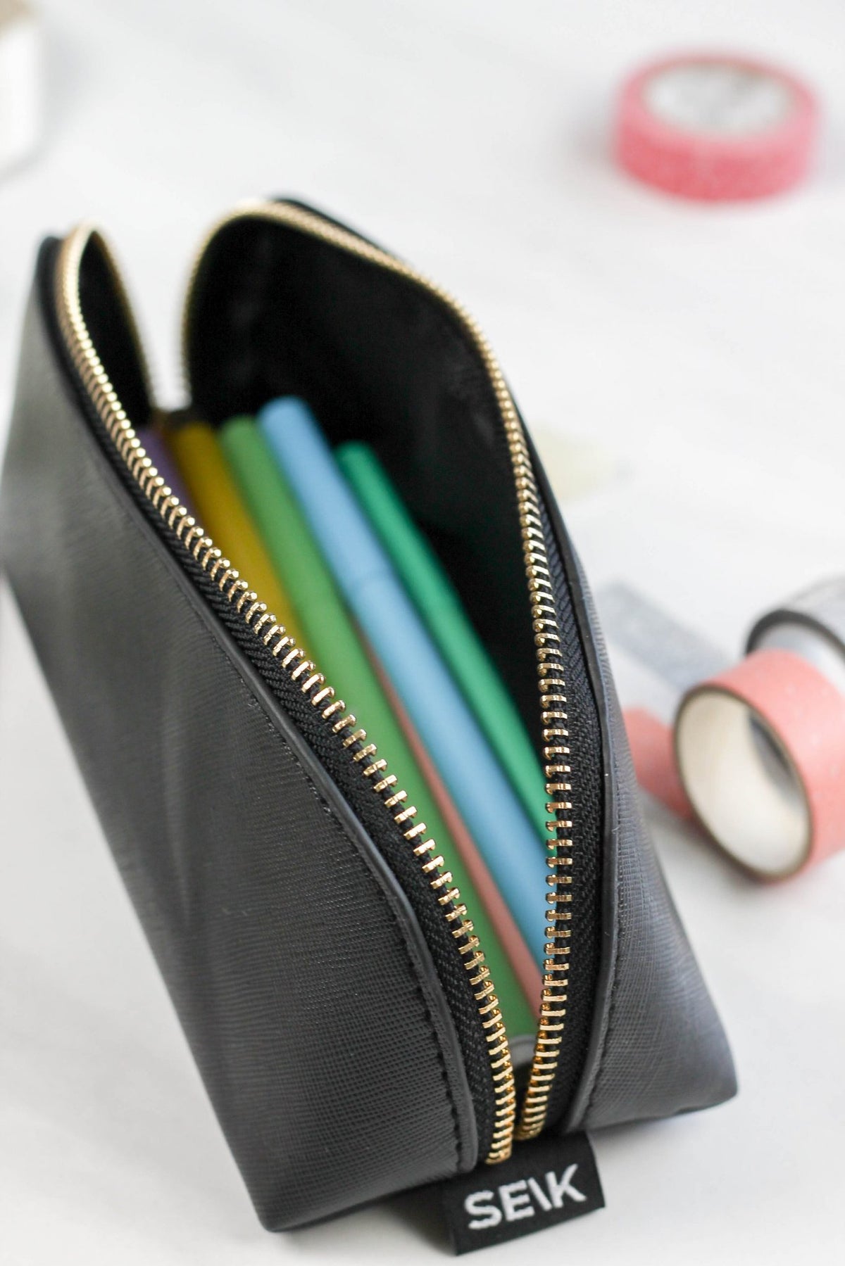 1. SEIK black pencil case with gold zipper, filled with colorful pens, shown in lifestyle setting