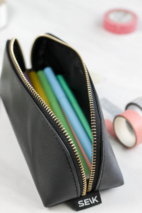 1. SEIK black pencil case with gold zipper, filled with colorful pens, shown in lifestyle setting
