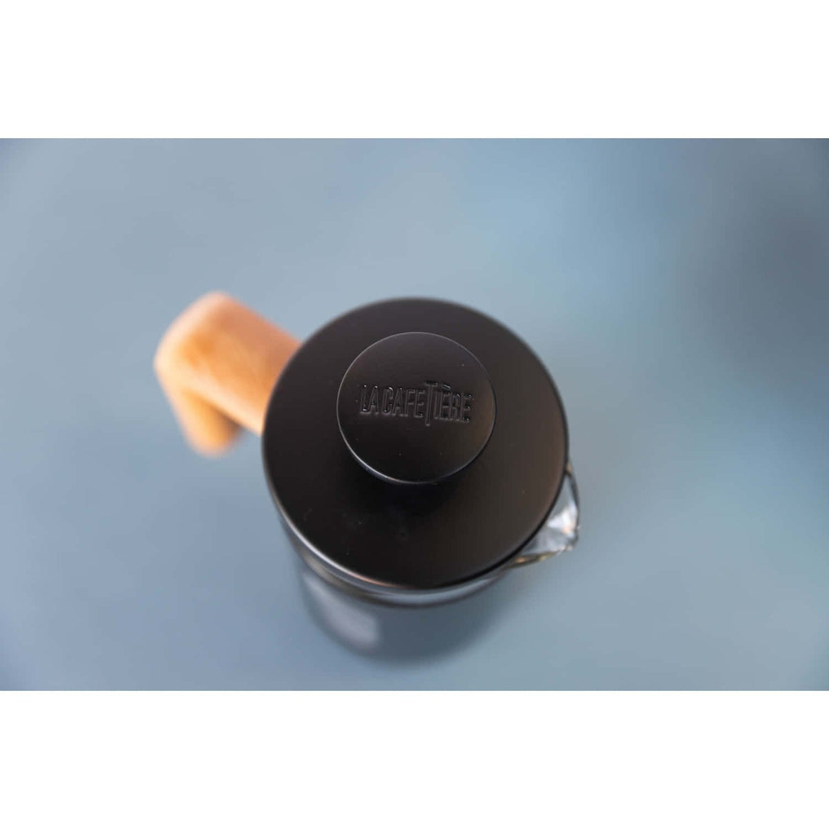 3. Top view of La Cafetière Pisa Coffee Maker lid with engraved logo and wooden handle on blue background