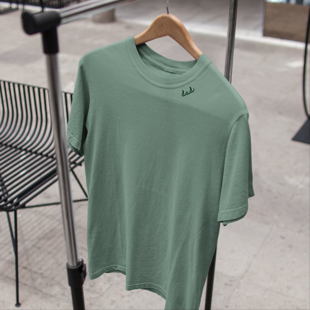 1. Unisex green organic cotton t-shirt with 'dad' embroidery on collar, hanging on a rack in a lifestyle setting