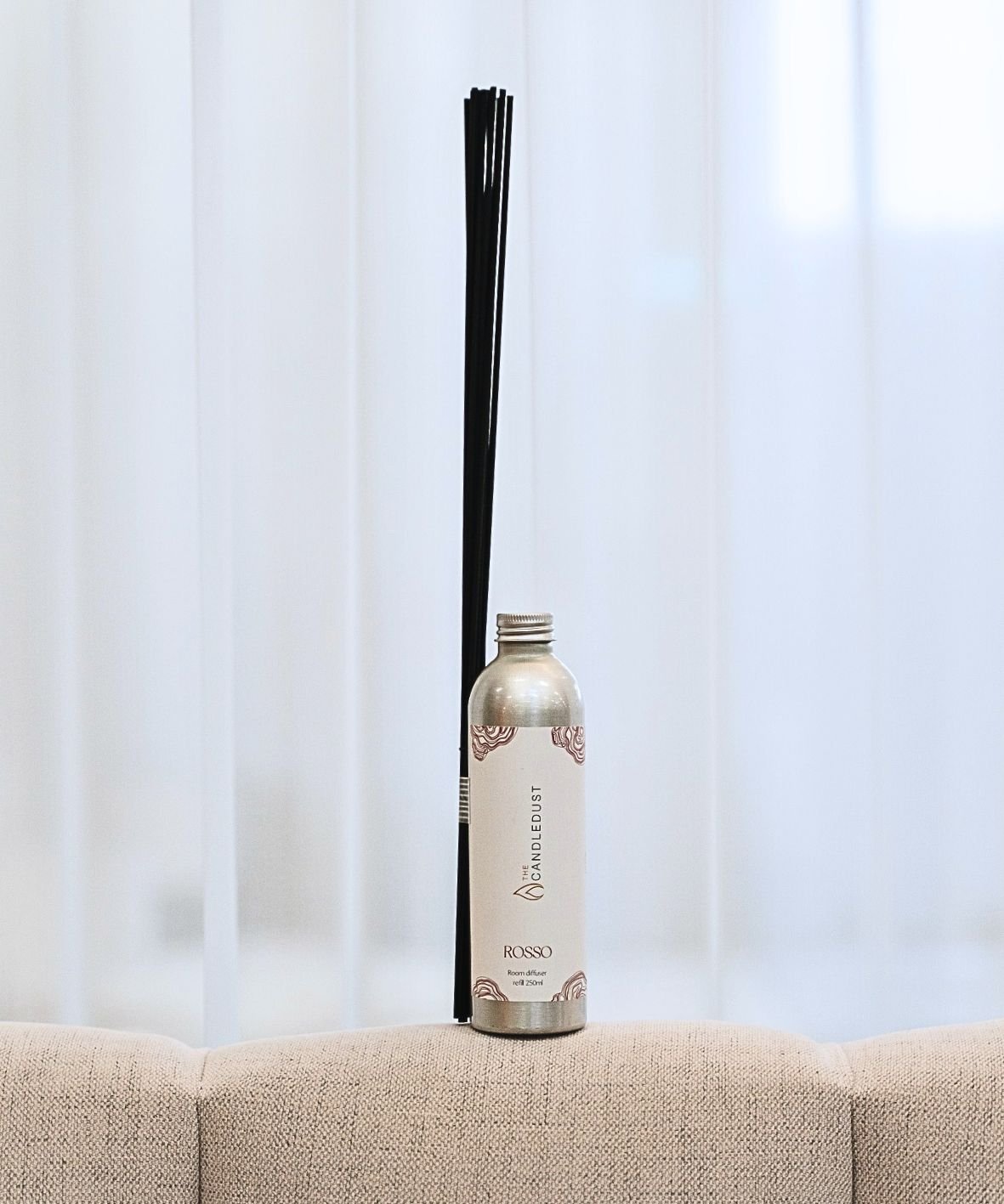 1. Candledust Rosso room diffuser refill with black reeds on a beige sofa, showcasing elegant design