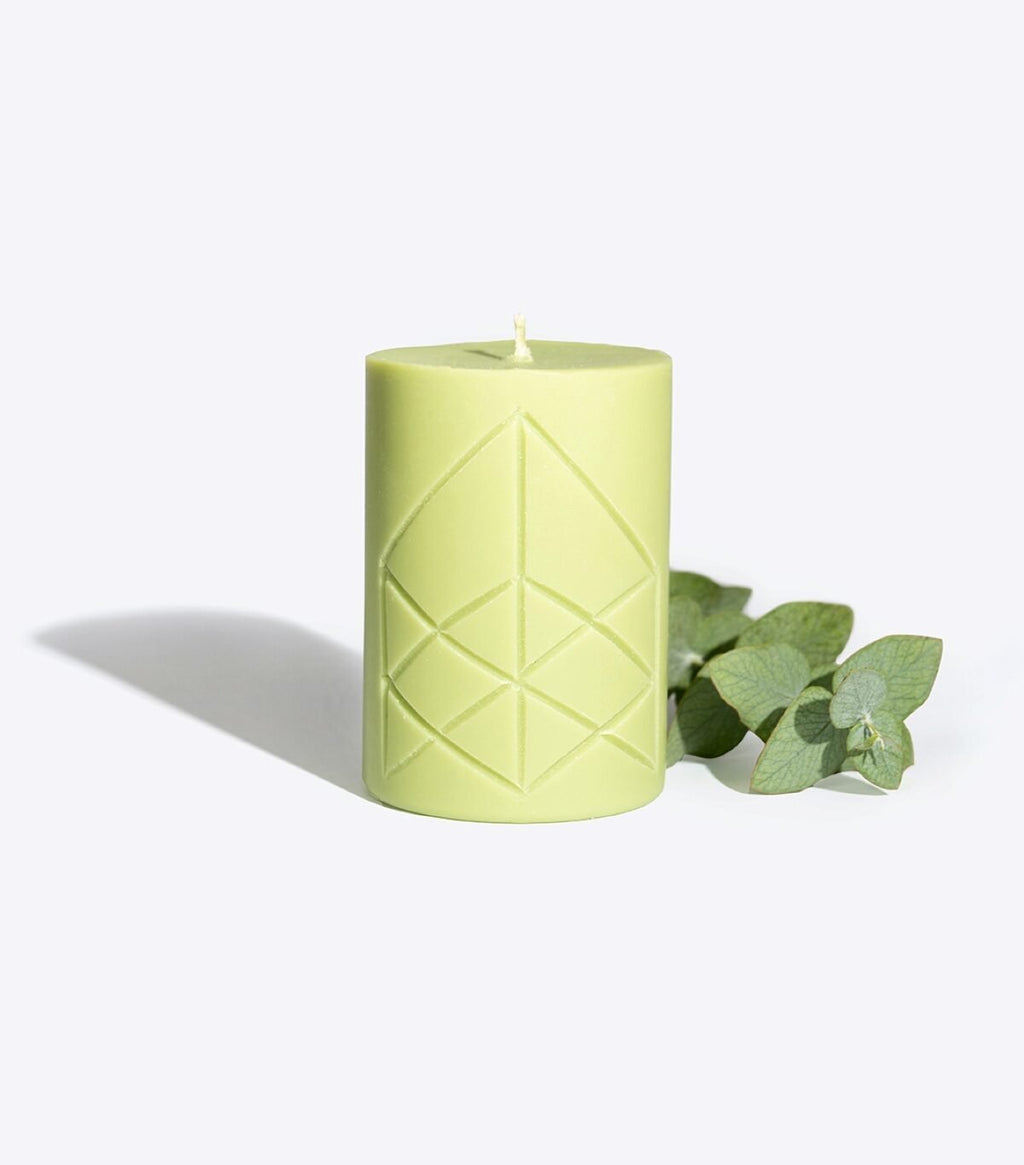 1. Smells Like Spells Rune Candle EIR in light green with rune design, shown with eucalyptus leaves, studio setting